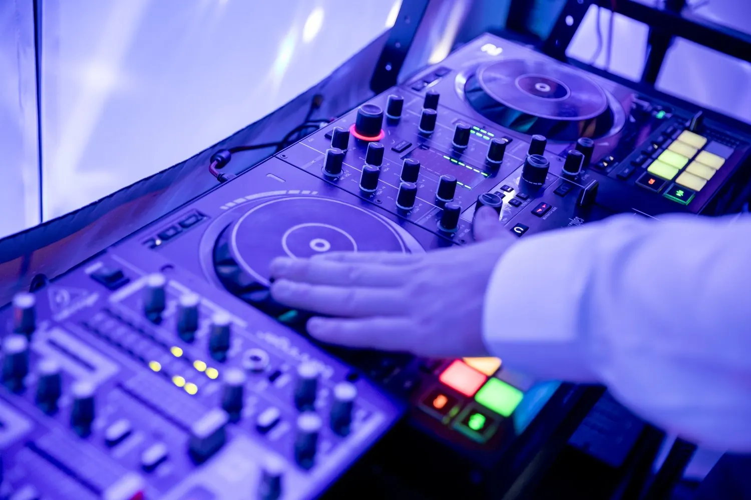 Hand am DJ-Controller, dahinter bunte Lichteffekte