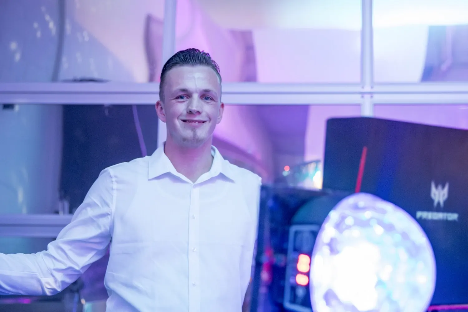 Hochzeits-DJ Nick Baumgarten lächelt in die Kamera, vor ihm Lichteffekte am DJ-Pult