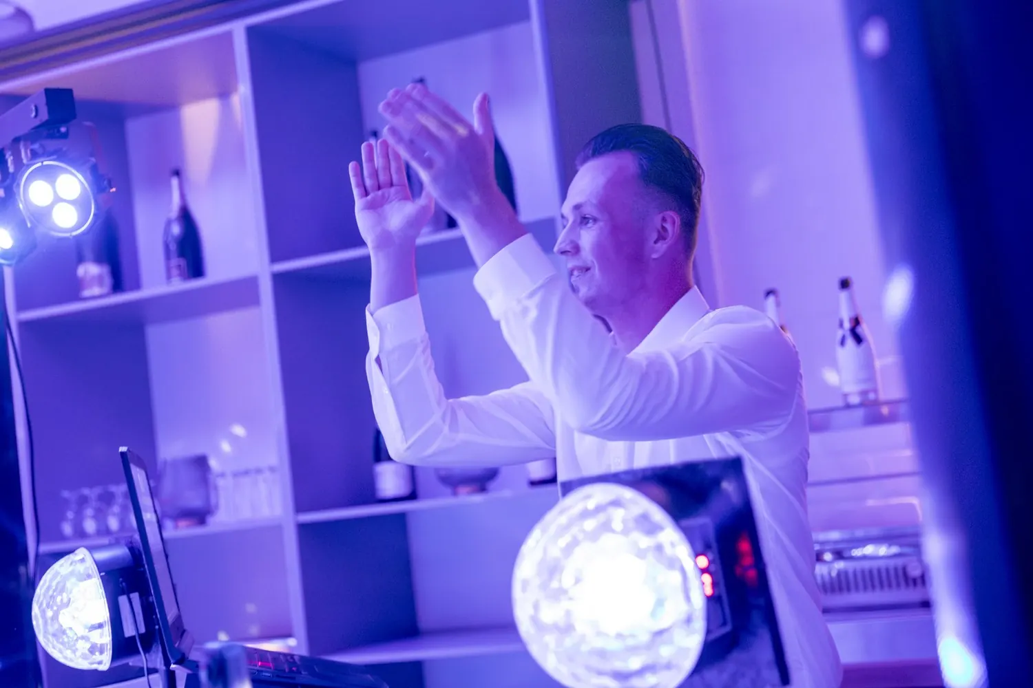 Hochzeits-DJ Nick Baumgarten klatscht am DJ-Pult in violettem Licht