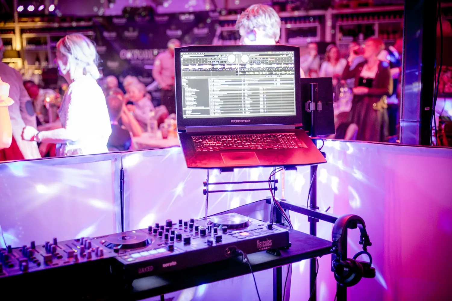DJ-Pult mit Controller und Laptop, dahinter feiernde Gäste