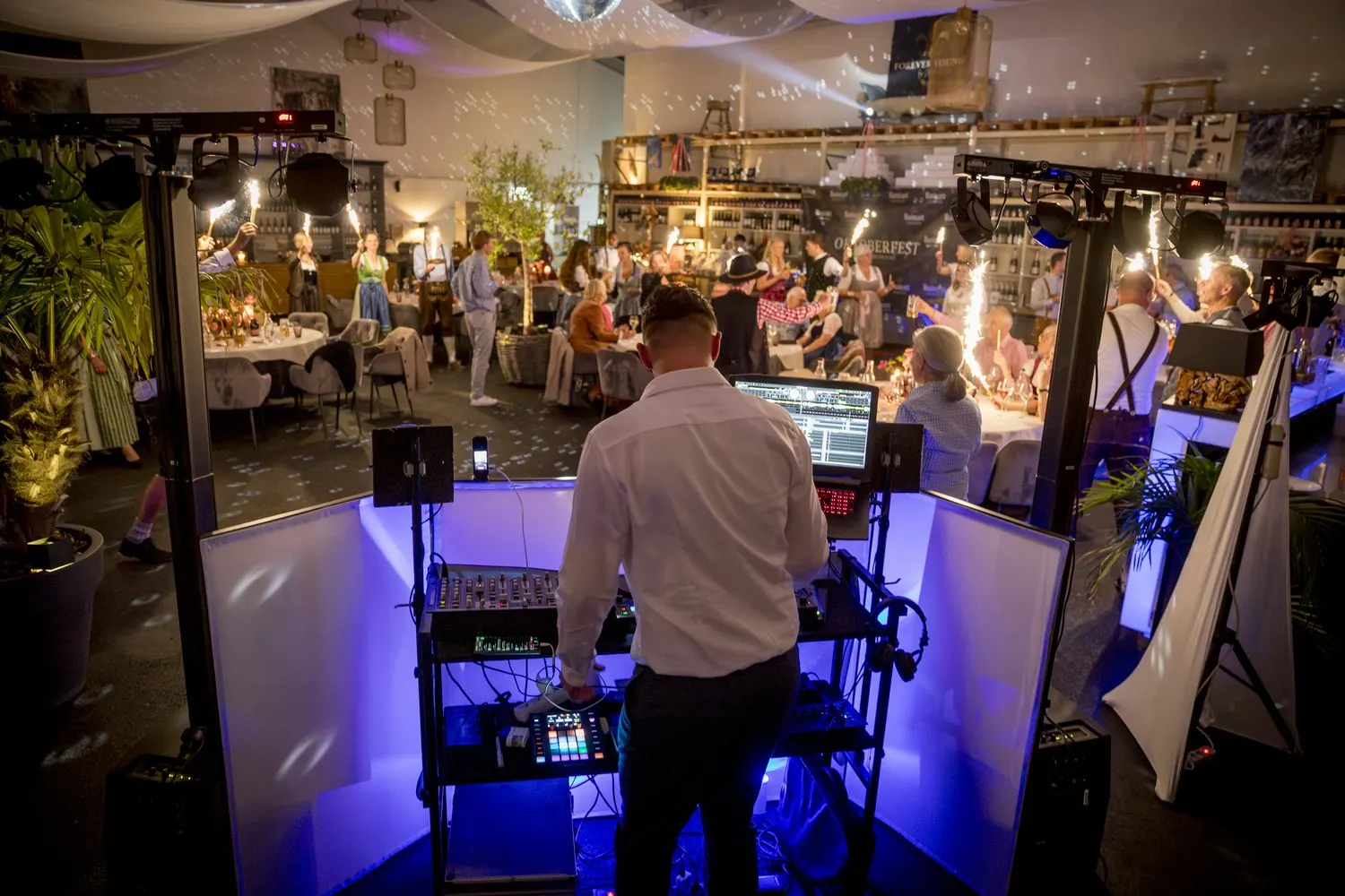 DJ Nick Baumgarten am DJ-Pult, vor ihm feiern die Gäste mit Wunderkerzen